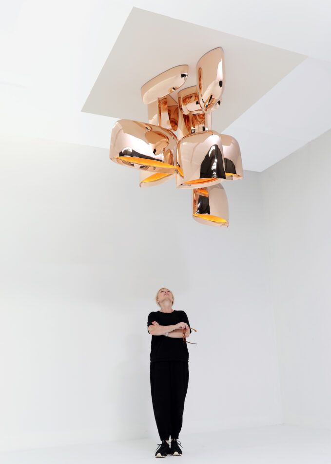 Furniture designer Niamh Barry in a white room looking up at her What If Everything Is Not Linear? light sculpture