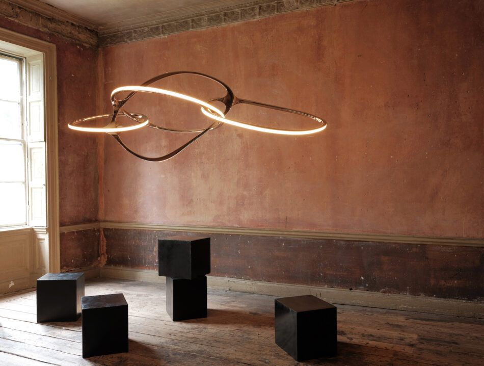 Niamh Barry On It Goes suspended light sculpture hanging by a window in a rustic room with terracotta-colored walls