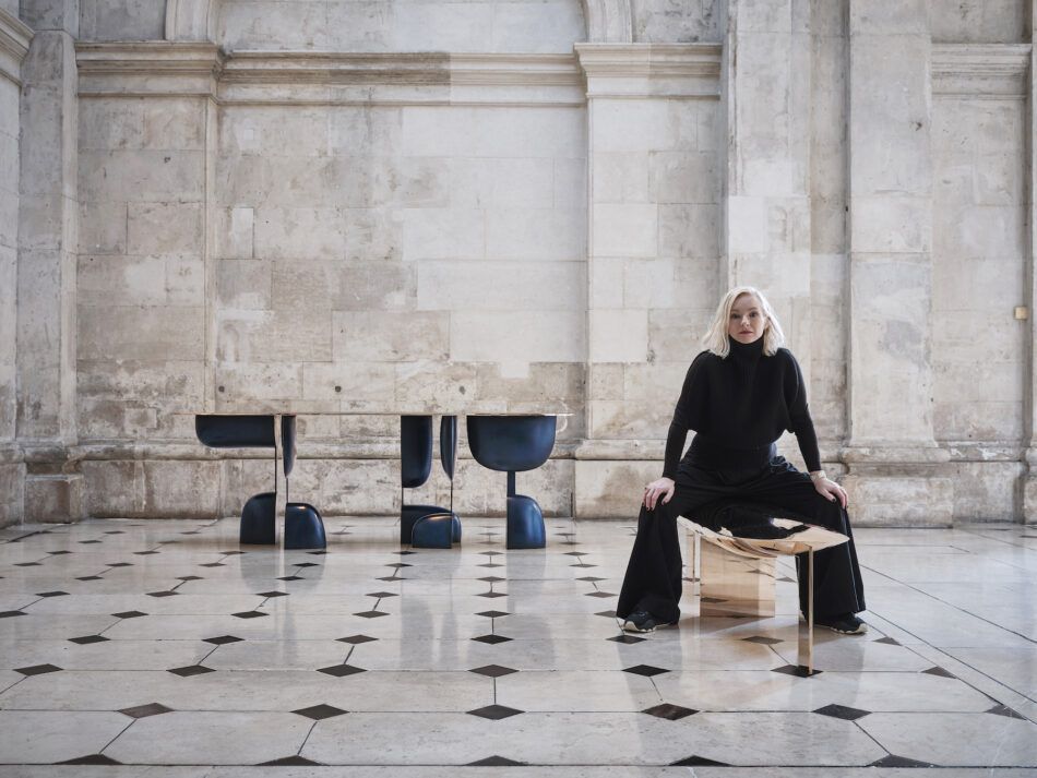 Furniture designer Niamh Barry sitting on her Ghost bench in the foreground with her Shouldering table in the background