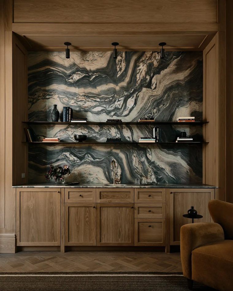 A slab of swirling green-and-white Fantastico marble rising behind steel floating shelves is framed a white-oak cabinet surround for a bar in Encion by Christina Cole Abboud