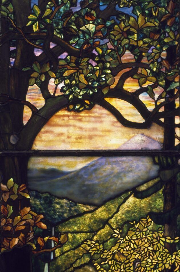 A stained-glass window showing a view of a mountain landscape between a pair of tall trees