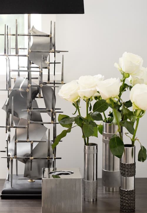 A brutalist lamp is balanced by sleek tubular vases holding white roses in this East Hampton bedroom designed by Timothy Godbold.