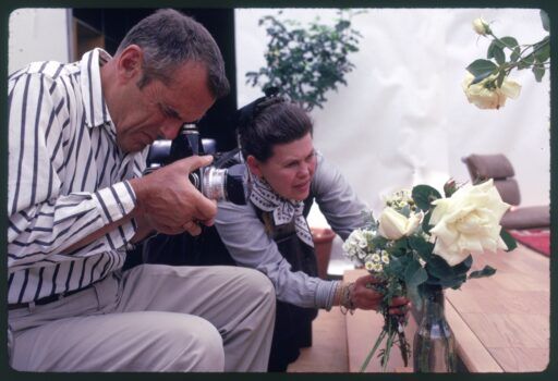 A photo of Ray Eames adjusting flowers as Charles Eames takes a photo of them
