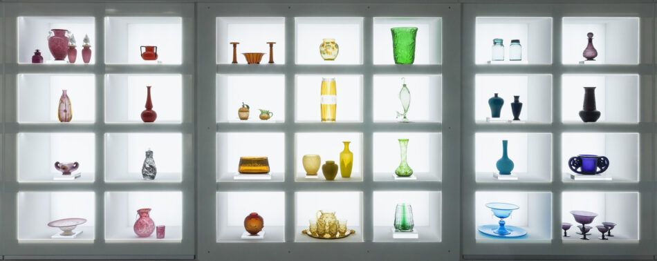An illuminated wall of glass objects arranged in rainbow order in the exhibition "Brilliant Color" at the Corning Museum of Glass