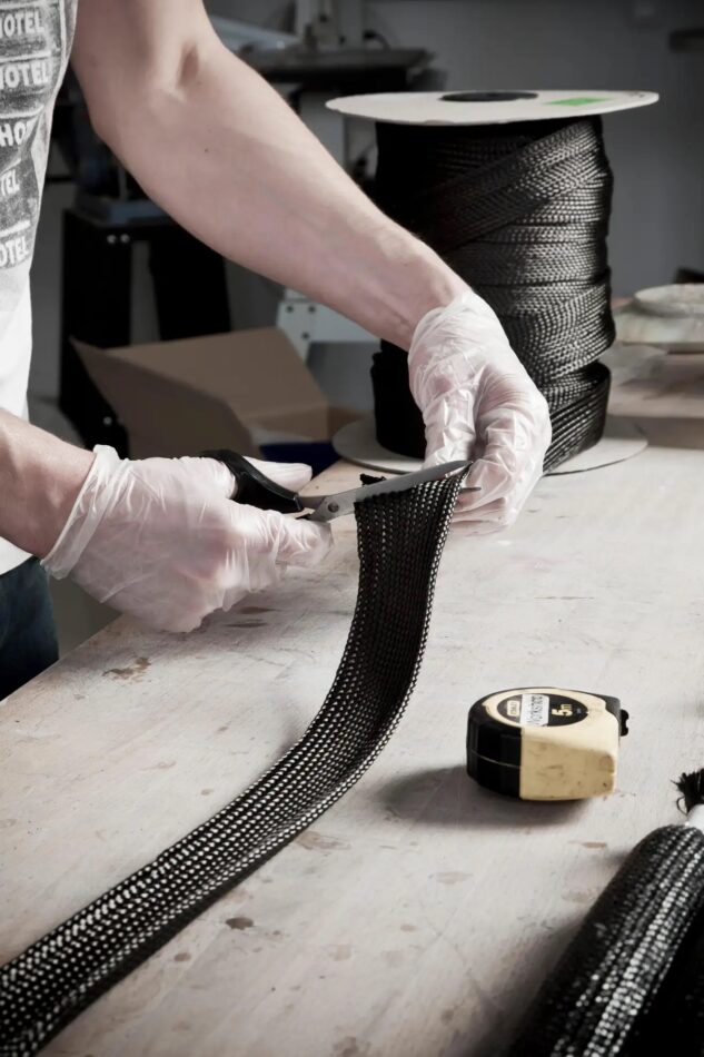 A craftsperson cuts a length of braided carbon fiber for the Marcel Wanders Carbon Balloon chair