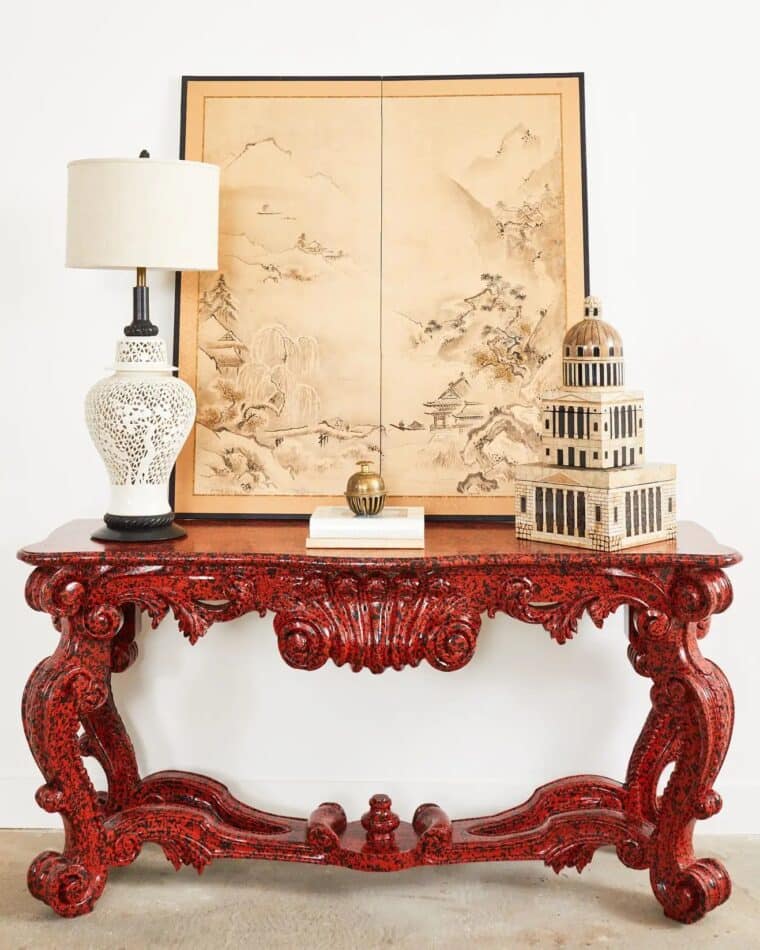 Ira Yeager rococo-style mahogany console table painted red and black and styled with a lamp, an Asian landscape artwork and other decorative objects on the tabletop.