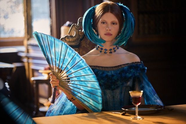 Mia Goth wearing a blue fan and a blue dress with a scarab necklace
