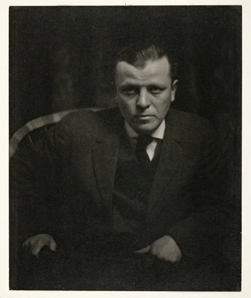 A black-and-white photograph taken by Alfred Stieglitz of painter Arthur Dove wearing a dark suit and leaning forward in a chair.