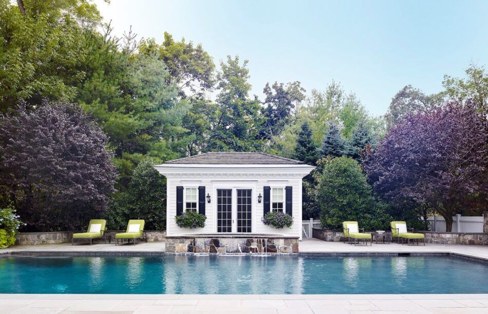 A white pool house designed by Douglas Graneto, with green chaises