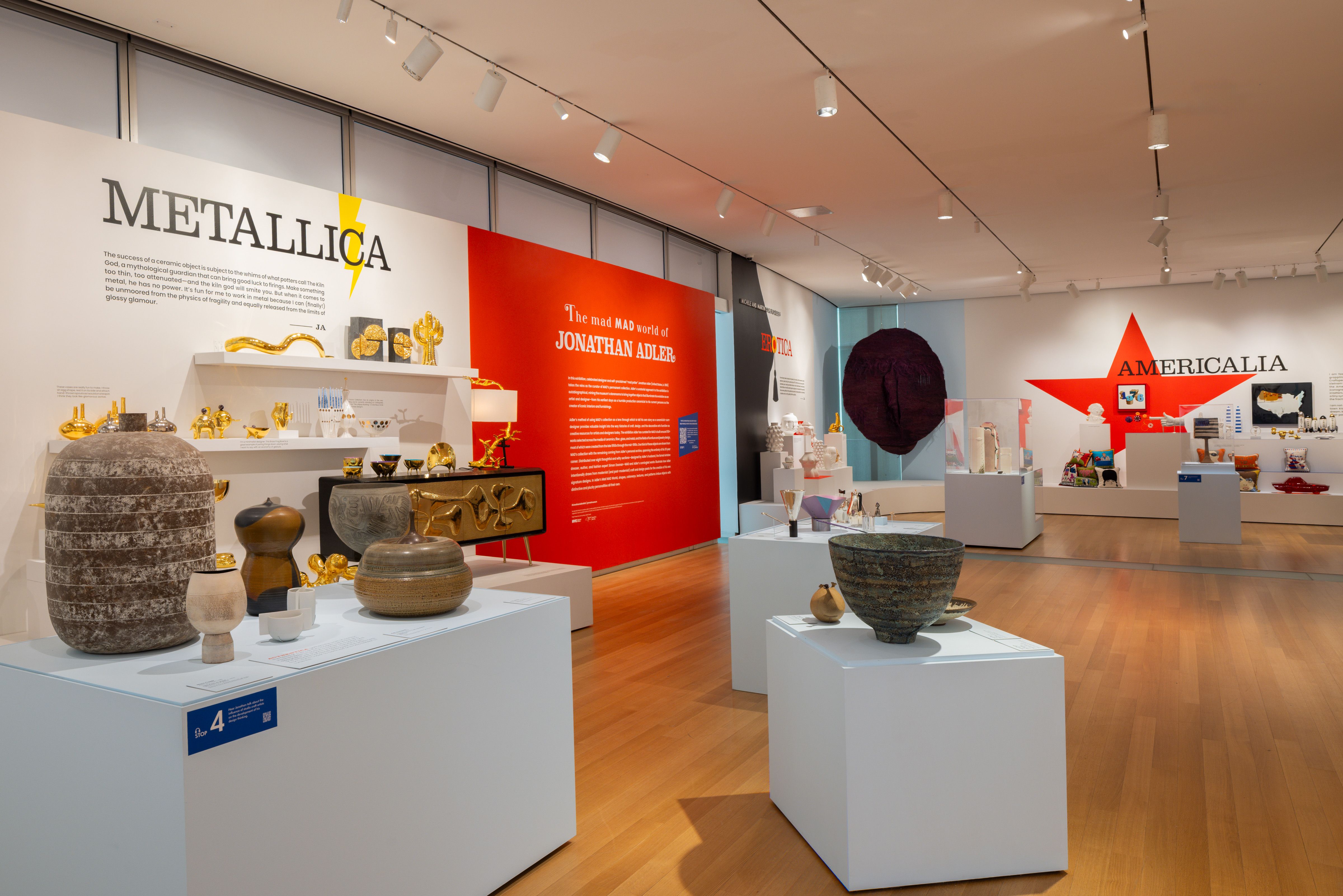 Gallery space with sections titled "Metallica" and "Americalia" with pottery on display on plinths and shelves.