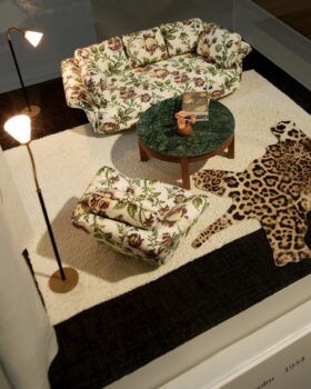 A miniature room with floral printed couch and armchair, wood table, and animal print rug