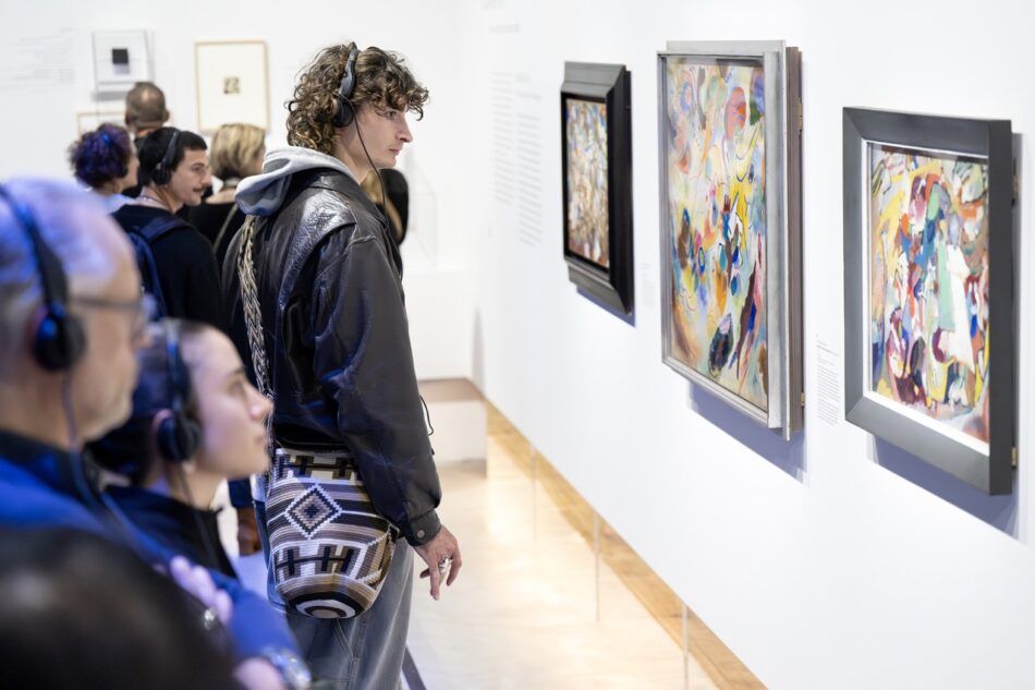 Museum goers wear headsets while looking at Kandinsky paintings