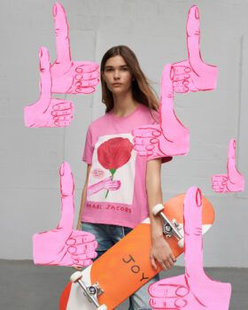 Image of model wearing a pink t-shirt with a David Shrigley drawing and holding an orange skateboard with the word JOY written on it