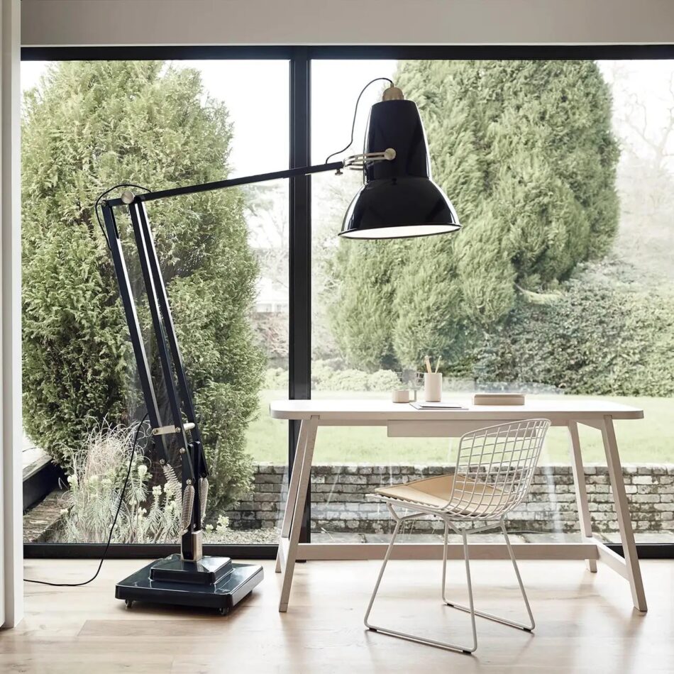 A giant Anglepoise Original 1227 floor lamp hovers over a desk facing a picture window