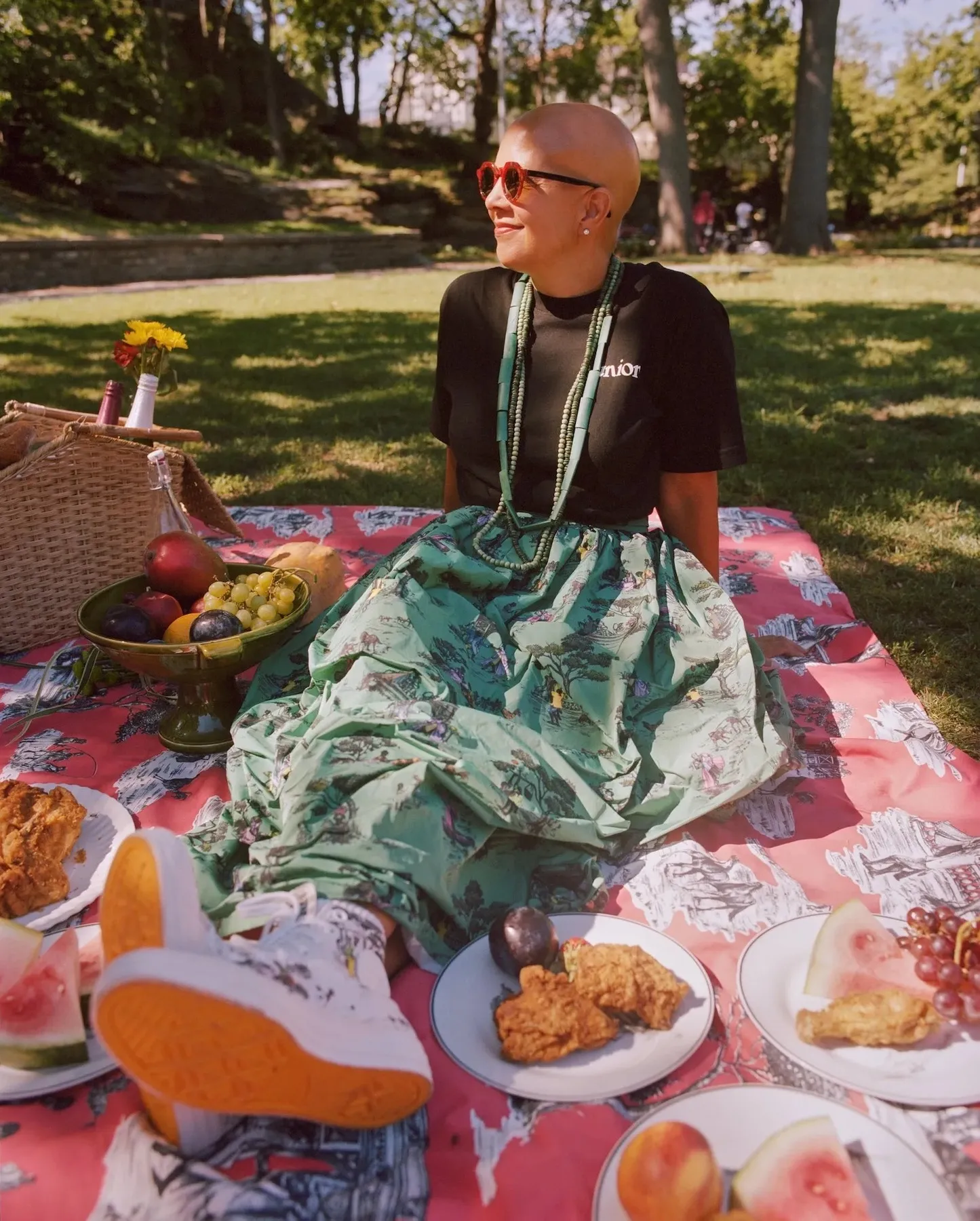 Interior designer Sheila Bridges rests on a picnic blanket made from her Harlem Toile fabric while wearing a skirt and sneakers featuring the same pattern.