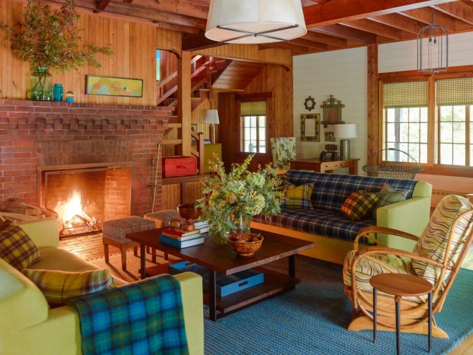 Living room with green sofas and plaid pillows and upholstery. Brick fireplace with small artwork above. 