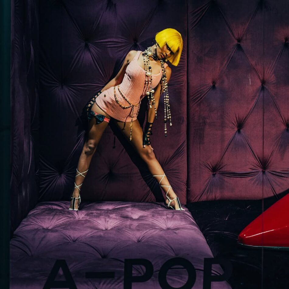 Tyla wears a yellow wig, draped pearl necklaces, a Chanel belt, and a pink Chanel top as a dress