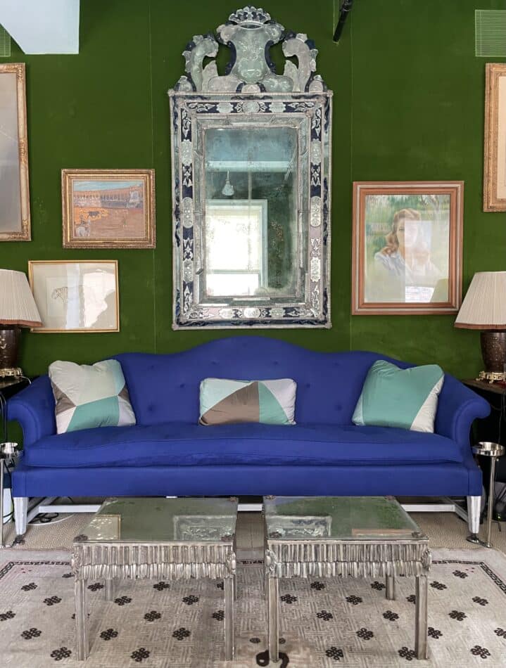 A Venetian mirror hanging over a blue sofa against a green wall in Miles Redd's office