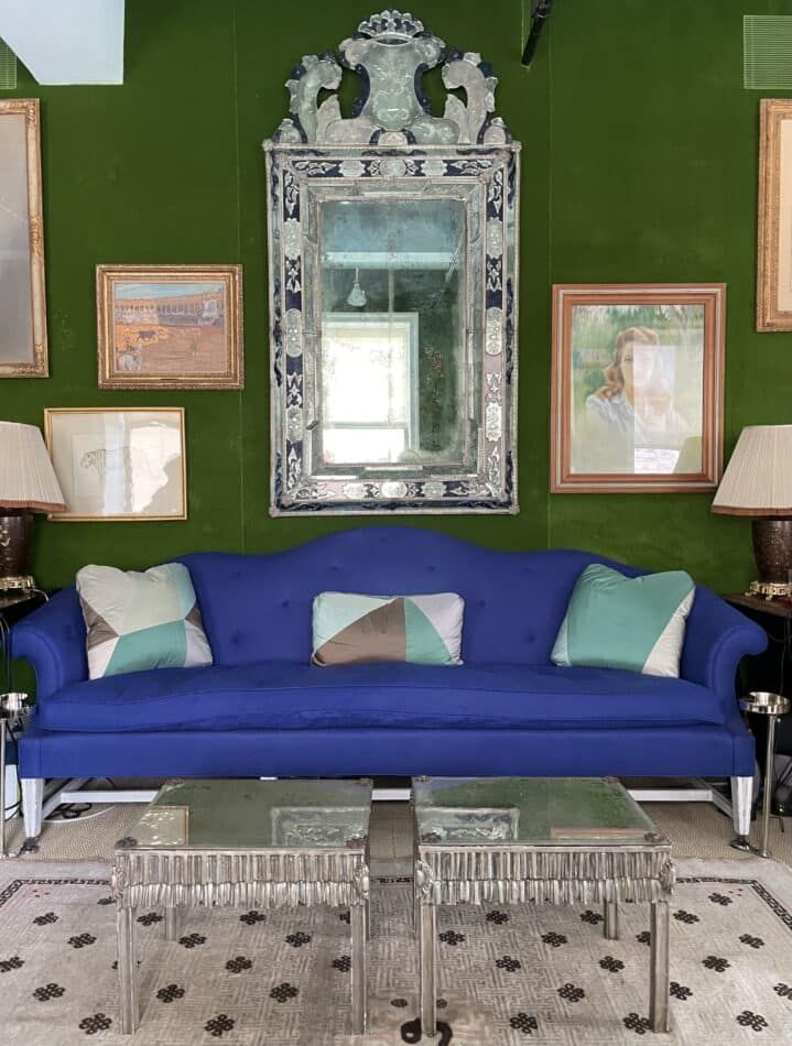 A Venetian mirror hanging over a blue sofa against a green wall in Miles Redd's office