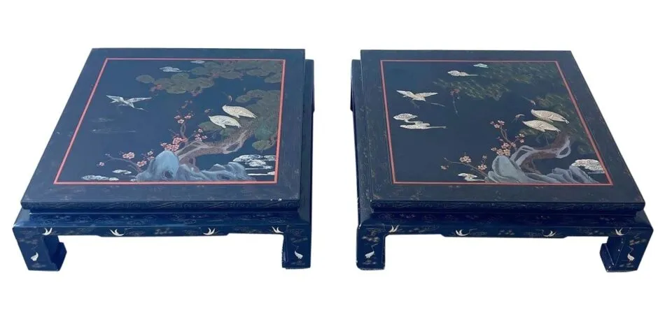 Two black square coffee tables sit side-by-side, each painted with leafy green trees and white cranes. 