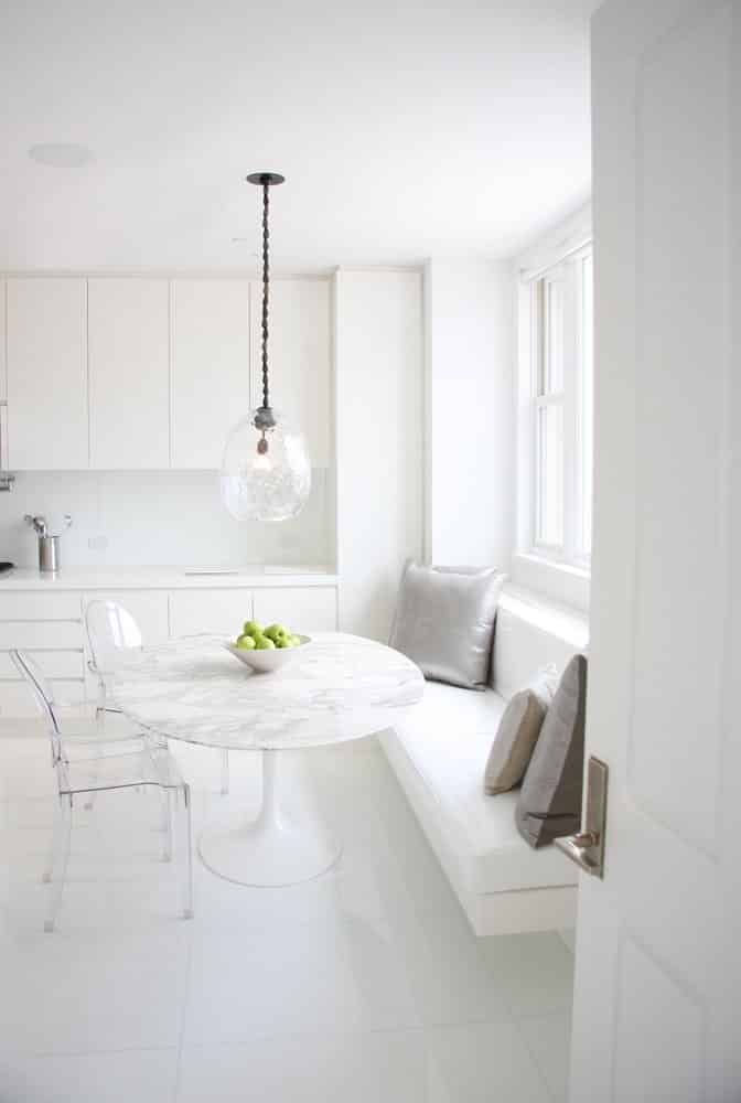 The all-white kitchen of a New York City penthouse by Kelly Behun features lucite chairs around an Eero Saarinen Tulip table. Photo by KBS