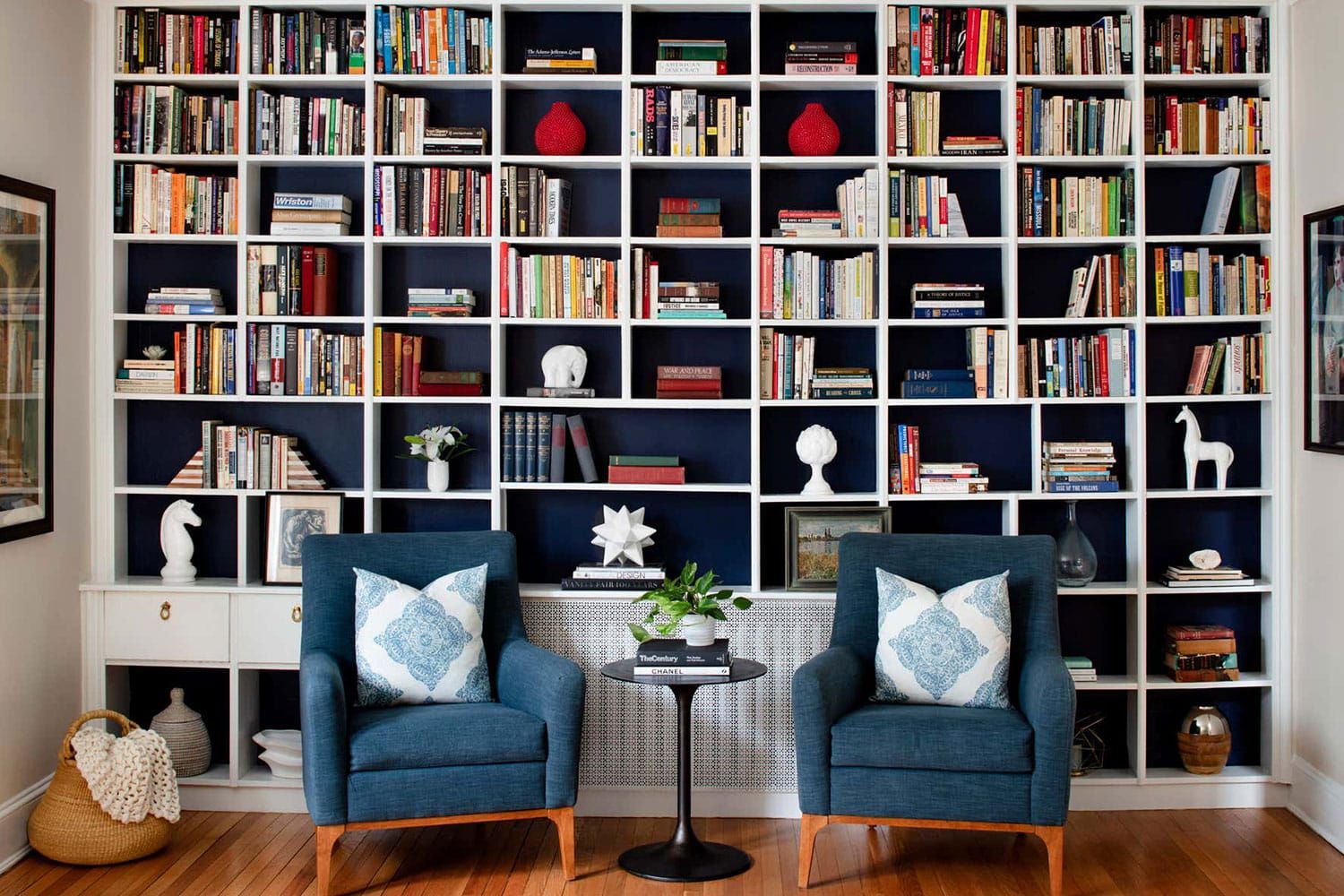 A color photograph of a Baltimore living room, designed by Laura Hodges Studio, that incorporates a floor-to-ceiling bookcase displaying the family's book and antiques collection. Photo by Jennifer Hughes