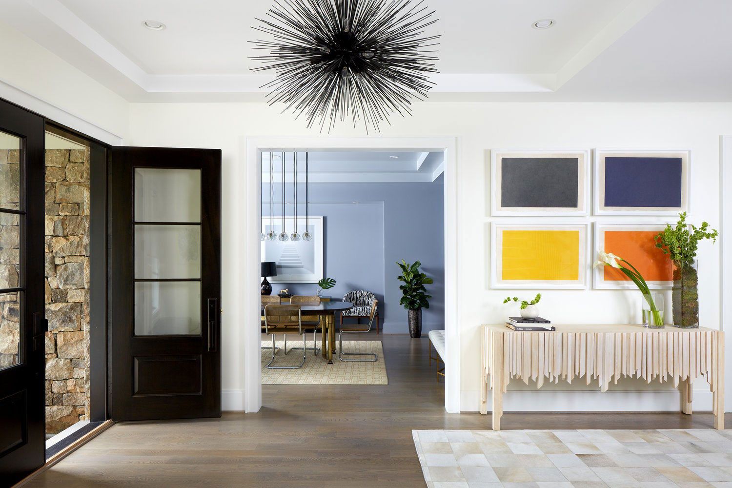 a home entryway with a black door and light fixture, with white walls and colorful art