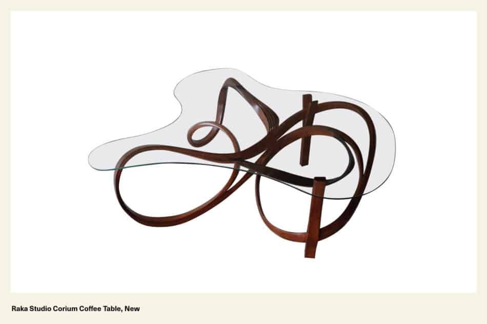 A Raka Studio Corium glass-top coffee table with a curved wood base.