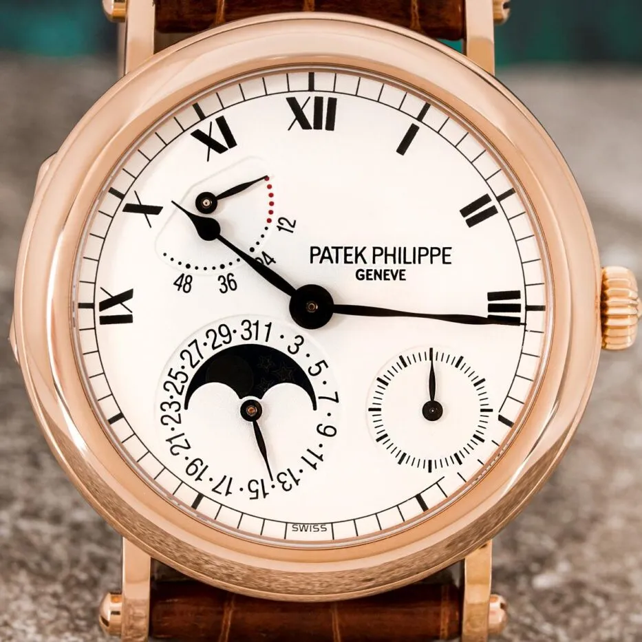 The white face of a Patek Philippe Moonphase Power Reserve watch has Roman numerals and subdials marking seconds and displaying the date, plus a moonphase indicator and power reserve. 