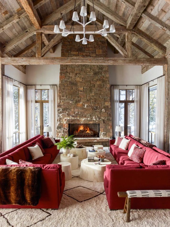 In the living room of a Big Sky ski chalet designed by Kylee Shintaffer, a J.T. Kalmar chandelier looms above a pair of red sectionals, which face bleached sycamore stumps used as tables.